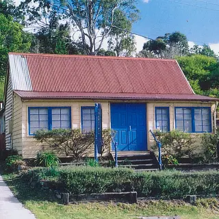 The façade, prior to re-construction, with original gable roof cladding and enclosed verandah